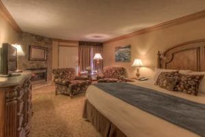 Spacious bedroom with two sitting chairs, fireplace, king-sized bed and grand dresser with tv.