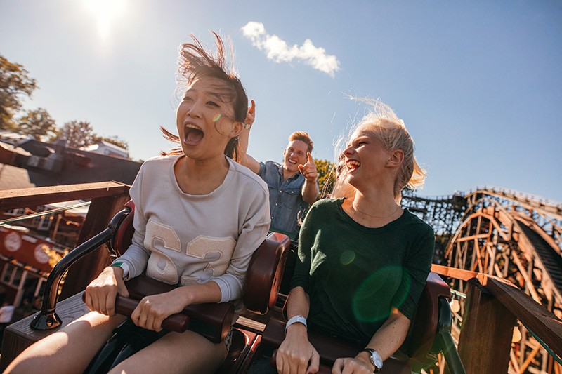 young women enjoying thrilling ride on wooden roller coaster
