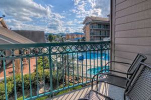 A small deck with green railing and two chairs overlooking a blue pool and hot tub.