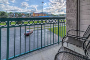 A small deck with green railing and two chairs overlooking parking lot.